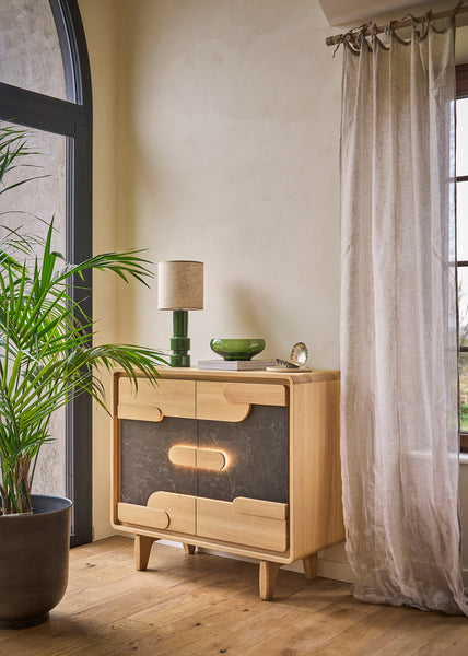 A mid-century modern wooden sideboard cabinet with ceramic inserts, optional lighting styled in a warm room next to a window with sheer curtains and a potted plant.