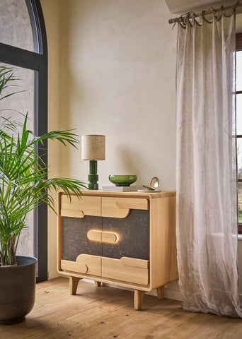 A mid-century modern wooden sideboard cabinet with ceramic inserts, optional lighting styled in a warm room next to a window with sheer curtains and a potted plant.