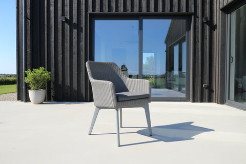 Rattan handwoven outdoor chair with Aluminium legs and waterproof seat pad on a modern patio in front of char clad modern house
