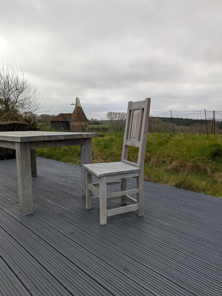 Wooden table and chair on a deck with a grassy field and cloudy sky in the background