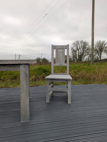 Gray chair on a wooden deck with a grassy field and trees in the background