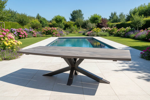 Wooden outdoor table in a garden with a pool and colorful flowers in the background