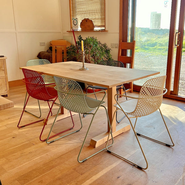 Dining area with a handmade Sussex solid oak fine table and colorful chairs near a large window.illar dining