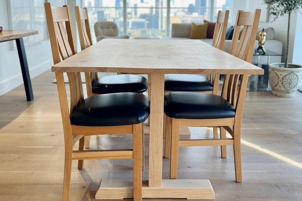 Dining area with Sussex handmade solid oak fine pillar dining table and westfield solid oak chairs in a room with a plant and wall art.