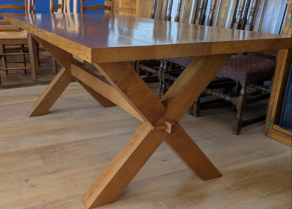Close-up of handmade oak cross leg dining table with chairs in a room with blue walls.