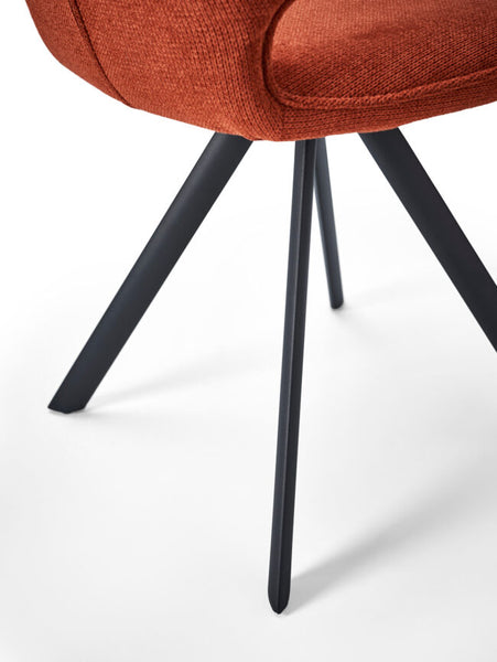 Close-up of an upholstered chair showing a rust-orange textured fabric seat cushion and matte black metal legs on a white studio background.