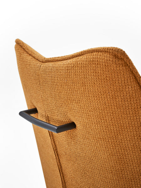 Close-up of a mustard yellow textured fabric chair back with a black metal handle, set against a plain white background.