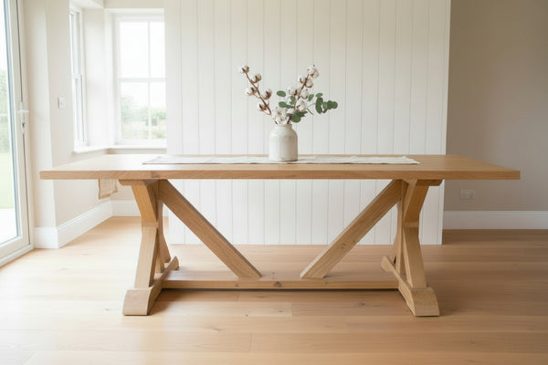 Cross braced oak dining table with a white ceramic vase in a modern farmhouse 