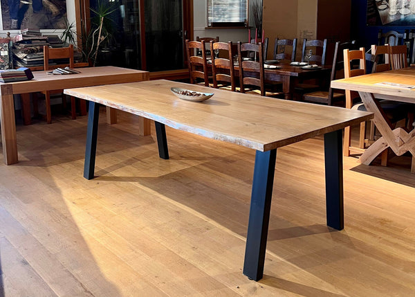 Handmade solid oak and steel table with waney live edge top in a showroom with other tables and chairs.