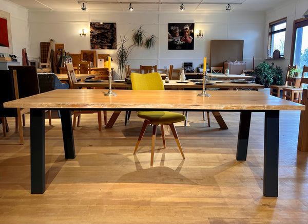 Large waney edge oak dining table with black legs in a room with chairs and decor