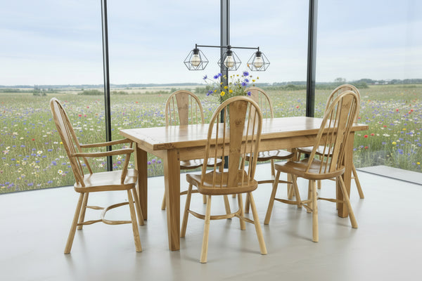 Handmade Sussex Farmhouse oak table with a set of ippy splat dining chairs in a room overlooking a wild flower meadow