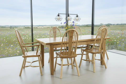 Handmade Sussex Farmhouse oak table with a set of ippy splat dining chairs in a room overlooking a wild flower meadow