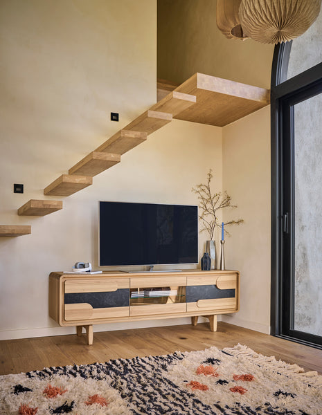 A modern light wood TV console, a black flat-screen TV, a patterned rug, and a large black-framed glass door.
