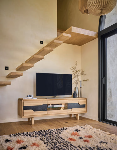 A modern light wood TV console, a black flat-screen TV, a patterned rug, and a large black-framed glass door.