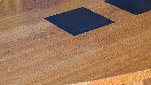 Close-up of a solid oak oval dining table with slate inserts against a blue wall