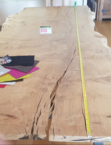 Large high character rare high character burr oak table top with waney edge with open knots, splits and cracks, being measured with a tape measure.