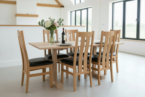 Side view of our handmade Sussex fine oak pillar dining table with a set of Westfield chairs with upholstered seats