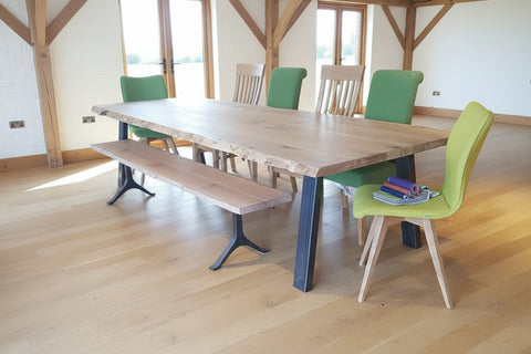 Live edge oak table on a steel base with bench and chairs in a modern barn conversion